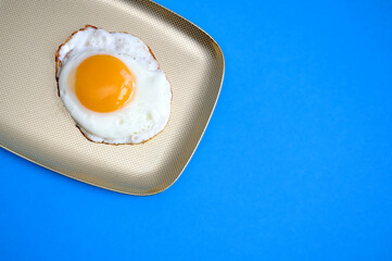 Fried eggs, scrambled eggs on a golden plate on a blue background in a food pattern. View from above. Minimalist food fashion concept.