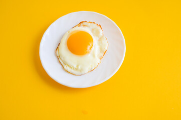 Fried egg on a white plate. Fried eggs on a yellow background. Breakfast