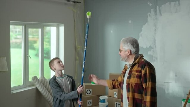 Grandpa planning repairs in apartment and explaining to grandson the amount of work. Eelderly man and young guy with paint rollers in hands against backdrop of an apartment in process of renovation.