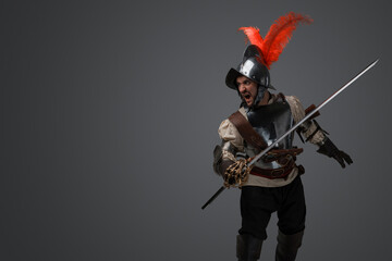 Studio shot of isolated on gray background soldier with epee dressed in plate armor.