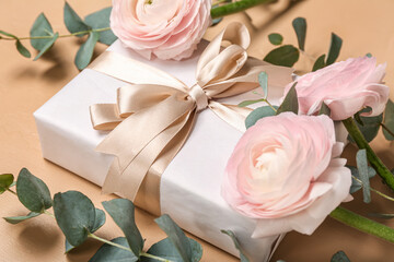 Beautiful ranunculus flowers, eucalyptus leaves and gift for Women's Day celebration on beige background