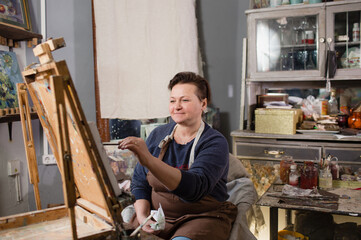 a professional female artist is engaged in painting on canvas in the studio. The artist paints a picture in her studio