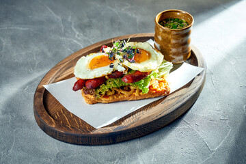 Sandwich with eggs with yolk, sausages on a board. Concrete background, morning light. Fried egg for breakfast.