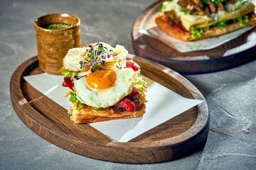 Sandwich with eggs with yolk, sausages on a board. Concrete background, morning light. Fried egg for breakfast.