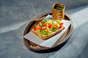 Toast with salmon, cherry tomatoes and lettuce on a wooden board. Concrete background, morning light. Food for breakfast