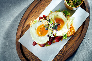 Toast with scrambled eggs with yolk, sausages on a board. Concrete background, morning light. Eggs for breakfast. Top view