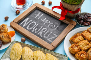 Chalkboard with text HAPPY NOWRUZ and treats on blue background, closeup
