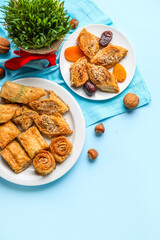 Plates with treats and grass on blue background. Novruz Bayram celebration
