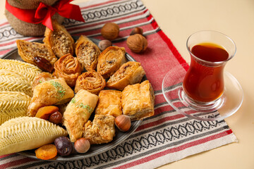 Plate with treats and glass of tea on beige background, closeup. Novruz Bayram celebration