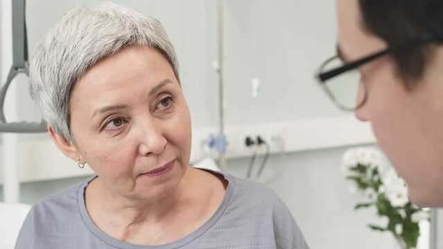 Medium closeup of short haired mature Asian woman and her doctor having conversation in hospital room