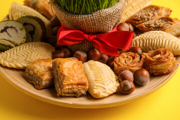 Plate with treats and grass on yellow background, closeup. Novruz Bayram celebration