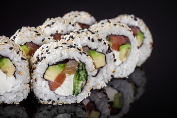 sushi roll with sesame avocado cucumber tuna and Philadelphia cheese on a black mirror background