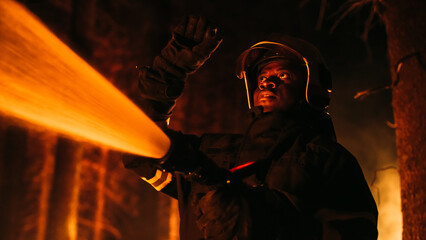 Close Up Low Angle Creative Portrait of a Brave African American Firefighter Using a Firehose to Fight a Forest Fire. Black Fireman Holds High-Pressure Water Hose, Battling Bushfire.
