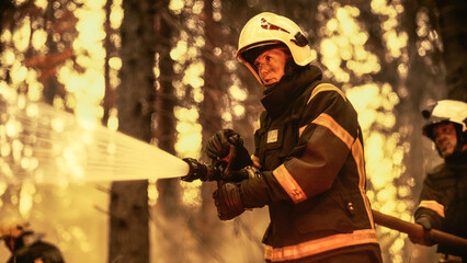 Team of Professional Firefighters Working on Wildland Fire Location, Extinguishing the Fire. Brave Female Firefighter in Safety Suit and Helmet Using a Fire Hose in Tandem with a Colleague.