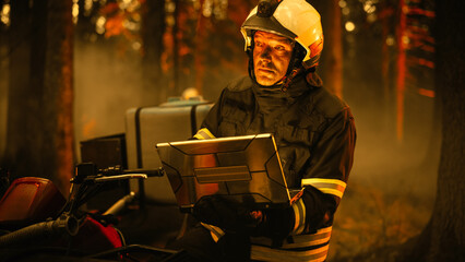 Portrait of a Handsome Fireman in Safety Gear Using Heavy-Duty Laptop Computer, Reporting on a...