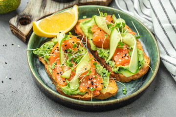 two toasts with salted salmon, guacamole avocado and fresh greens on plate. superfood concept....
