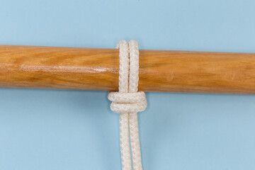 Rope Piwich knot tied around wooden pole on blue background