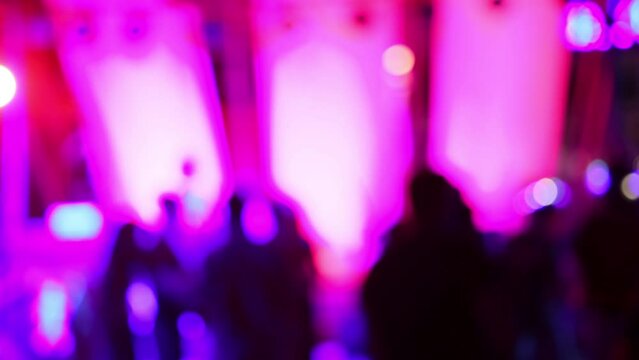 Blurred silhouettes of crowd of people dancing on the dance floor of a night club under the light of colored spotlights and lasers.