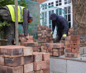 Two construction workers laying bricks as part of a renovation of an Edwardian suburban house in...