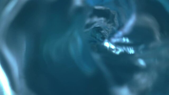 A whirlpool of blue water forming a spiral funnel with a round hole. Swirling of the surface of a transparent liquid with different speeds of rotation. Water tornado, cyclone. Macro shot, top view.