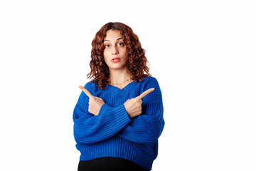 Millennial woman wearing blue knitted sweater standing isolated over white background crosses arms and points sideways, chooses between two options. Shocked, an incredible choice.