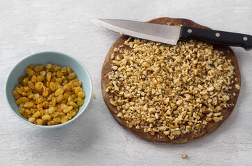 Wooden board with chopped nuts and a bowl of raisins, ingredients for making a cupcake or pie on a light gray background, top view. Cooking delicious homemade food