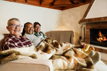 Multiracial friends having fun in front of cozy fireplace at home - Focus on left woman senior woman face