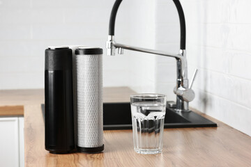 A glass of clean fresh water and set of filter cartridges on wooden table in a kitchen interior....