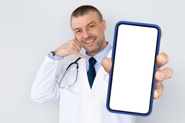 Middle aged male doctor showing blank smartphone and making call me gesture