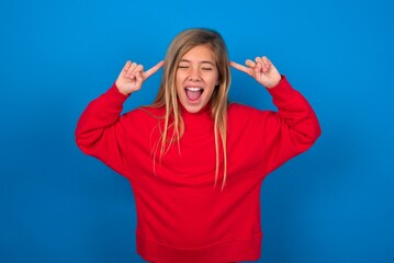 Fototapeta premium Photo of crazy caucasian teenager girl wearing red sweater over blue background screaming and pointing with fingers at hair closed eyes