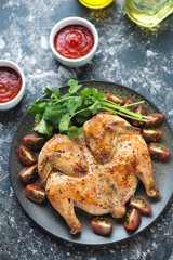 Chicken tabaka with fresh cilantro and dipping sauces, vertical shot on a dark-brown granite background, high angle view