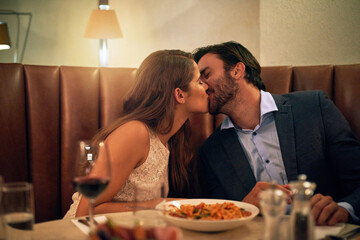 Happy couple, kiss and love for dinner date, embrace or relationship affection at night in restaurant. Man kissing woman lips in romance for fine dining, celebration or anniversary on valentines day