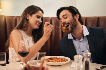 Romantic, date and woman feeding man spaghetti for dinner, supper and fine dining at a restaurant together. Couple, cute and happy lovers enjoying food, pasta and wine for valentines day