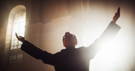 Portrait of Christian Priest Raising Hands In Blessing His Congregation while Praying In Church,...