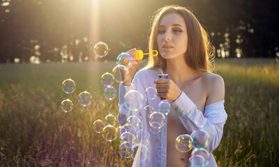 Beautiful young woman blowing soap bubbles in a field on a beautiful summer day	
