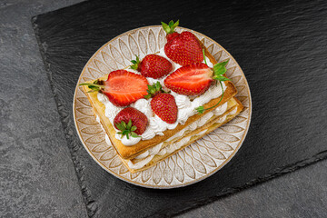 Puff pastry cake with whipped curd cream and fresh strawberries on a black background