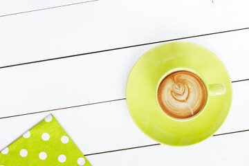 cappuccino coffee in green cup,   with napkin at polka dots scattered on white painted wooden table, top view - 569162900