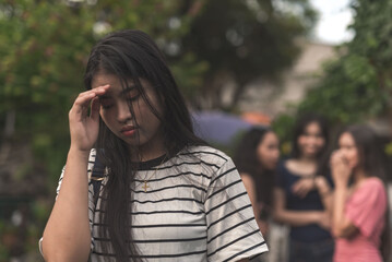 A emotionally hurt woman holds her forehead in shame while 3 women talk and gossip behind her back....