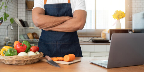 Man in kitchen looking at recipes on laptop while cooking