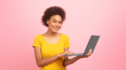 Glad smiling pretty young black curly lady working on laptop, enjoy study and work remotely