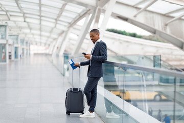 Fototapeta premium Smiling Black Businessman Messaging On Smartphone While Waiting Flight At Airport