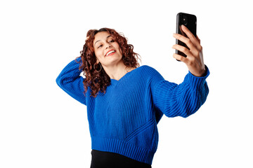 Cheerful woman wearing blue pullover sweater isolated over white background touching hair while taking selfie on mobile phone. Takes photos for social media.
