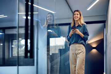 Smiling businesswoman standing in modern office with smart phone