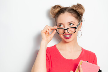 the portrait of young blondie caucasian woman with two hair bundles, glasses for vision, braces smiling widely and holding some notebooks; young woman businessman concept 