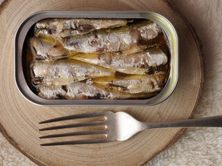 A can of sardines preserve and a fork on a wooden board. Top view.