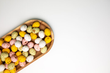 Multi-colored chocolate decorative eggs in wooden tray on a white background. Happy Easter background. Flat lay