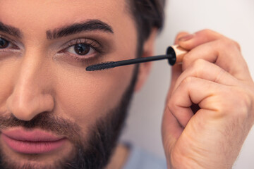 Modern young Caucasian man applying eye cosmetics