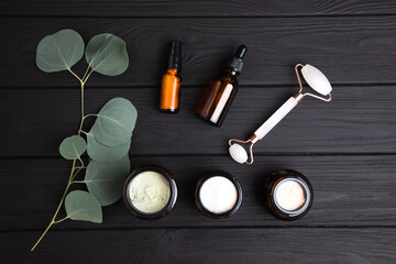 Amber bottles with facial cosmetics with a branch of eucalyptus on the dark wooden background. Top view