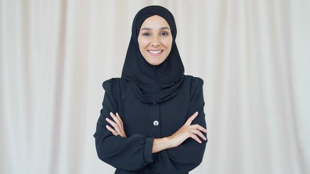 closeup portrait of a pretty young Muslim woman in a black hijab standing and smiling indoors at home Headshot of an Islamic happy female looking at the camera on a light room background close up