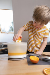 The child joyfully prepares freshly squeezed citrus juice in a glass